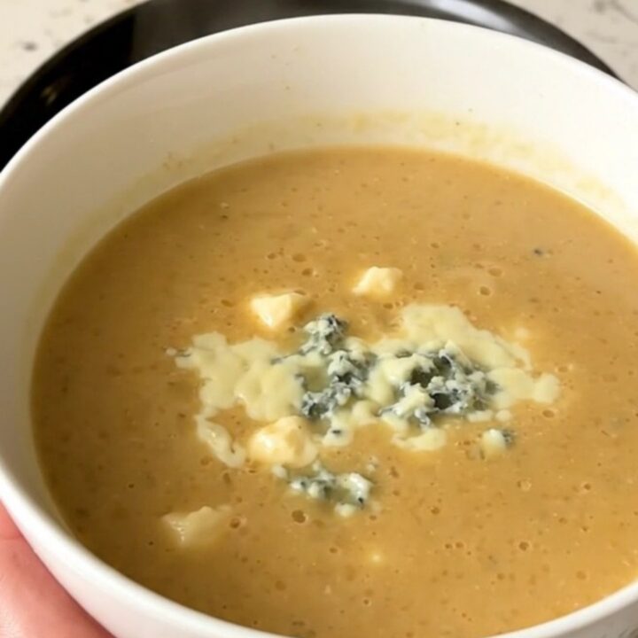 A close-up of a white bowl filled with creamy, smooth parsnip and pear soup topped with blue cheese.