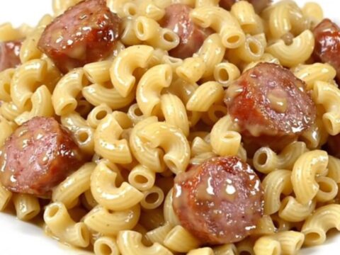 A steaming bowl of macaroni and sliced sausage in a white wine sauce, served on a white plate.