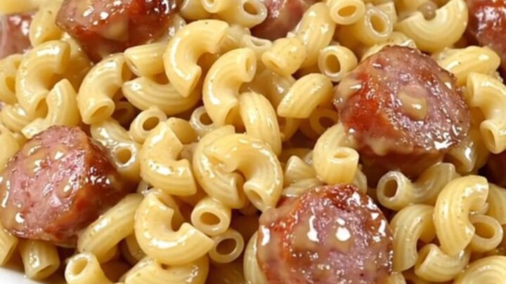 A steaming bowl of macaroni and sliced sausage in a white wine sauce, served on a white plate.