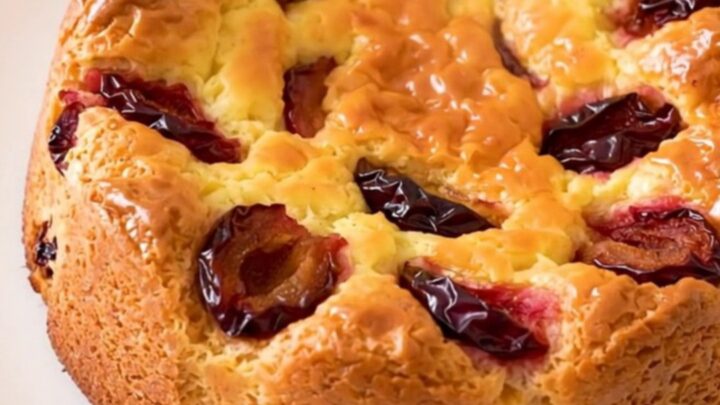 A golden, freshly baked plum clafoutis in a slow cooker on a white speckled countertop.