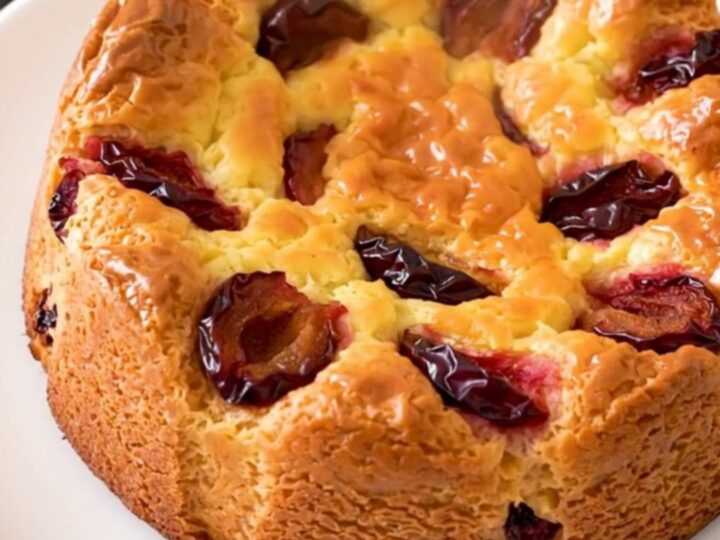 A golden, freshly baked plum clafoutis in a slow cooker on a white speckled countertop.
