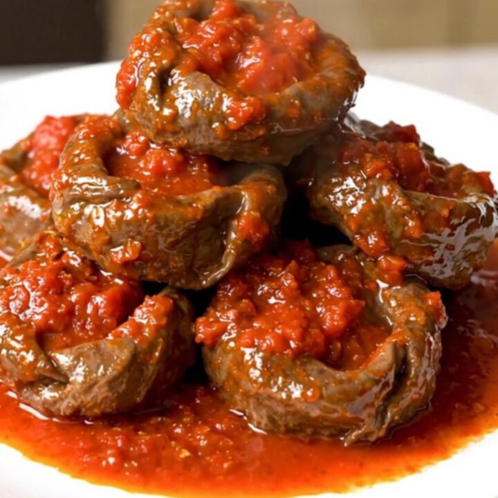 A close-up of tender veal paupiettes cooked in a rich, glossy tomato and herb sauce inside a slow cooker.