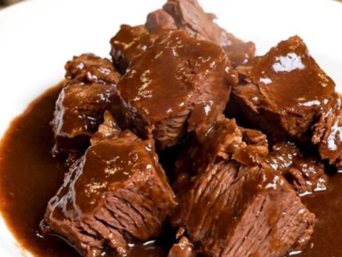 A rustic bowl of slow-cooked beef daube with carrots and mushrooms in a deep red wine sauce.