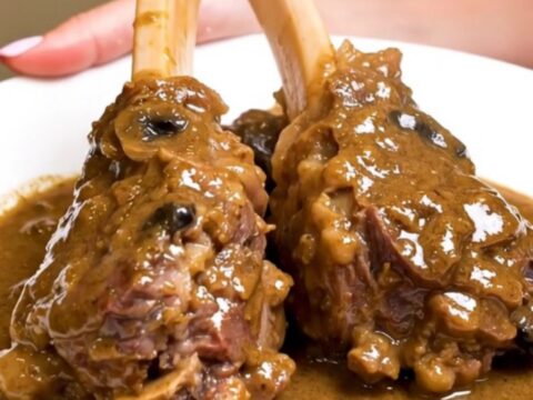 Two tender lamb shanks coated in a creamy mushroom sauce on a white plate.