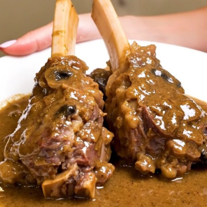Two tender lamb shanks coated in a creamy mushroom sauce on a white plate.