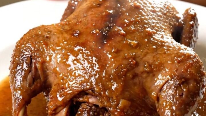 A close-up shot of a tender, glossy guinea fowl dish served on a white plate.