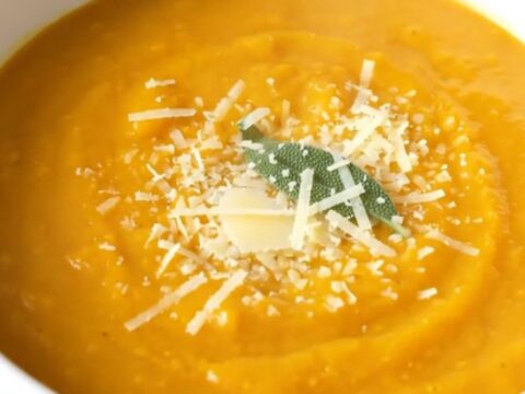 A warm, creamy bowl of butternut squash soup topped with grated parmesan and a fresh sage leaf.
