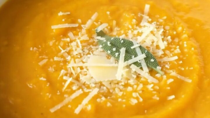 A warm, creamy bowl of butternut squash soup topped with grated parmesan and a fresh sage leaf.