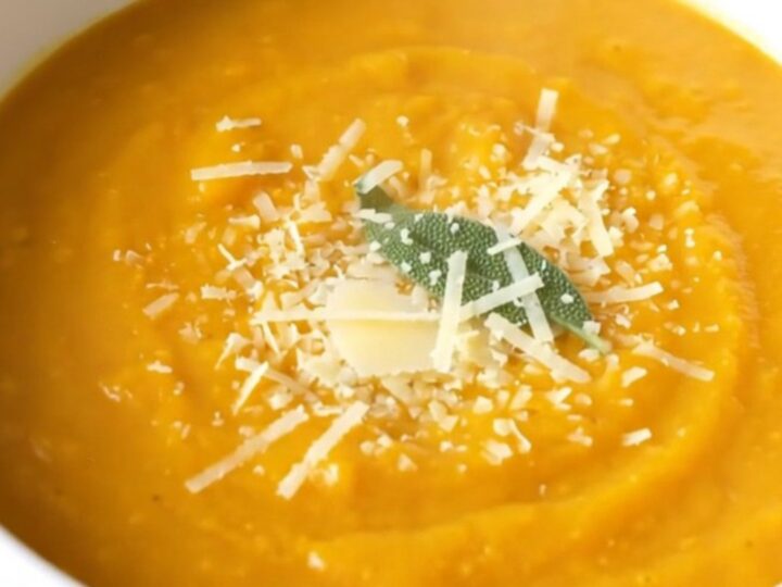 A warm, creamy bowl of butternut squash soup topped with grated parmesan and a fresh sage leaf.