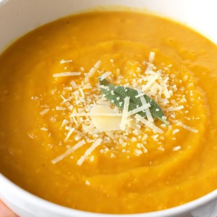 A warm, creamy bowl of butternut squash soup topped with grated parmesan and a fresh sage leaf.