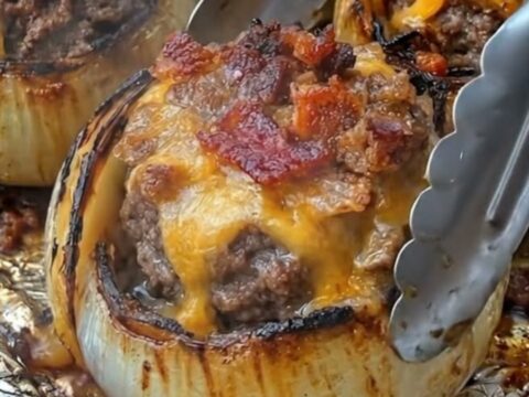 A close-up view of roasted stuffed onions with bubbling melted cheddar and crispy bacon.