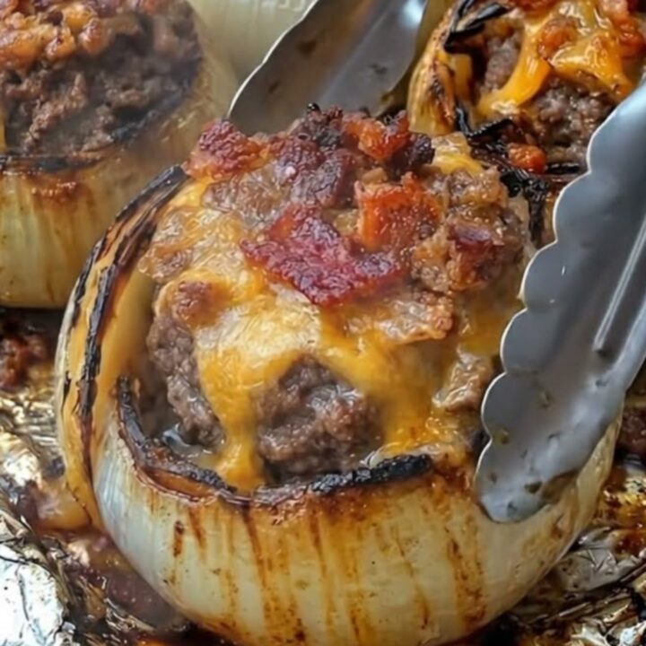 A close-up view of roasted stuffed onions with bubbling melted cheddar and crispy bacon.