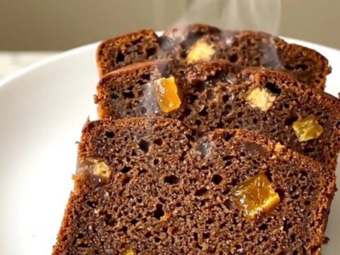 A sliced, spiced gingerbread loaf with candied orange peel on a white plate.