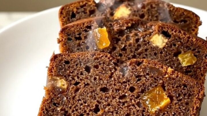A sliced, spiced gingerbread loaf with candied orange peel on a white plate.