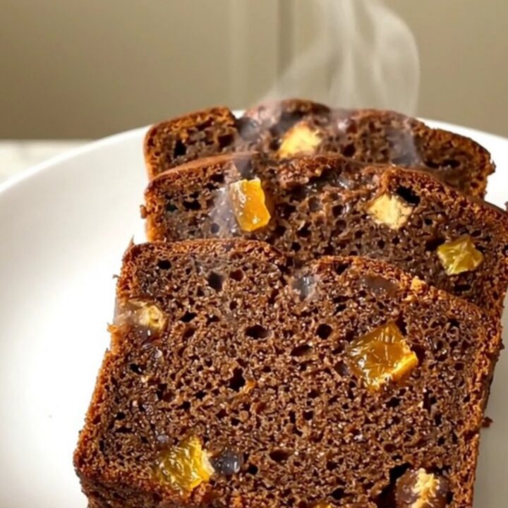 A sliced, spiced gingerbread loaf with candied orange peel on a white plate.