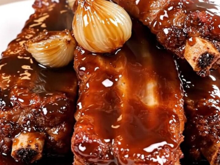 Slow cooked pork ribs with caramelized shallots and a dark balsamic glaze on a plate.