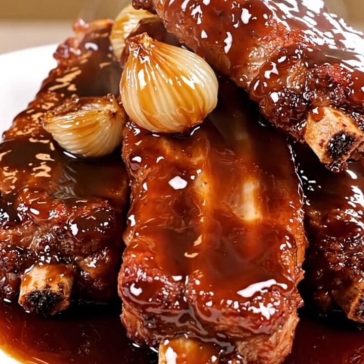 Slow cooked pork ribs with caramelized shallots and a dark balsamic glaze on a plate.