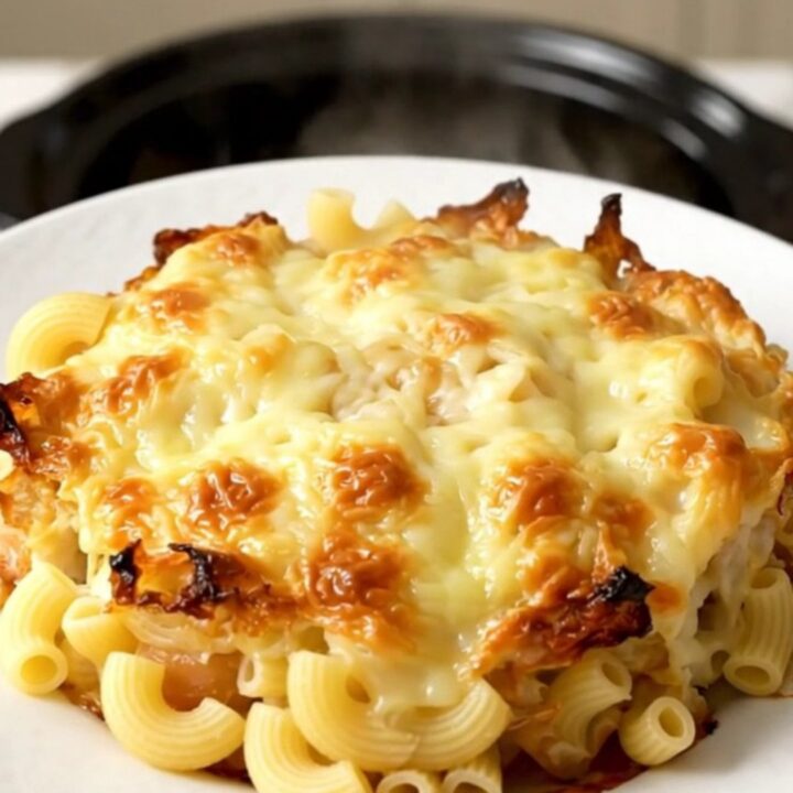 A close-up view of the creamy macaroni gratin in a slow cooker with visible melted cheese and bacon pieces.