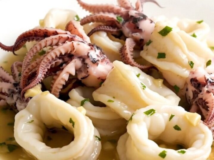 A top-down view of raw squid, sliced onions, and garlic in a black slow cooker on a white quartz countertop.