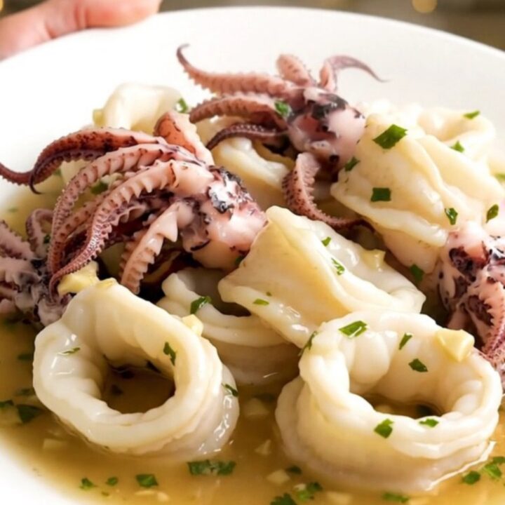 A top-down view of raw squid, sliced onions, and garlic in a black slow cooker on a white quartz countertop.
