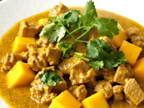 A close-up of slow cooker mango coconut pork curry served on a white plate with a garnish of cilantro.