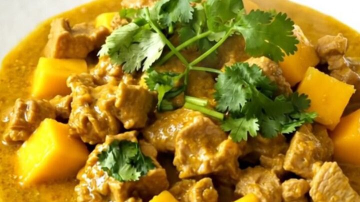 A close-up of slow cooker mango coconut pork curry served on a white plate with a garnish of cilantro.