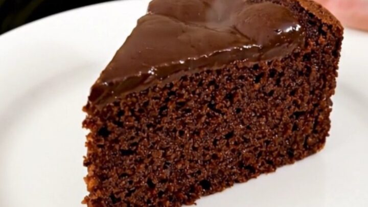 A warm, glossy slice of dark chocolate semolina cake served on a simple white plate.