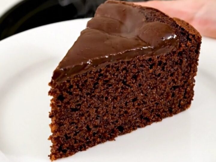 A warm, glossy slice of dark chocolate semolina cake served on a simple white plate.
