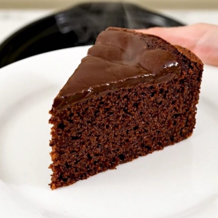 A warm, glossy slice of dark chocolate semolina cake served on a simple white plate.