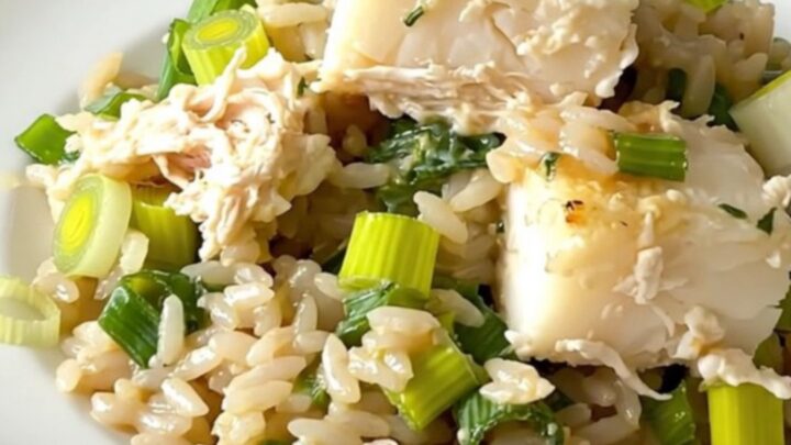 A top-down view of a black slow cooker filled with layers of fresh cod, sliced leeks, and uncooked white rice.