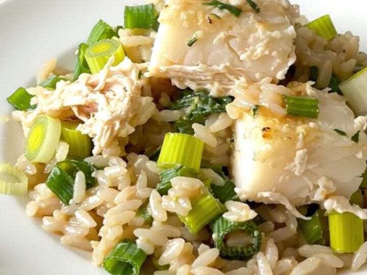A top-down view of a black slow cooker filled with layers of fresh cod, sliced leeks, and uncooked white rice.