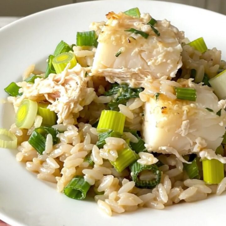A top-down view of a black slow cooker filled with layers of fresh cod, sliced leeks, and uncooked white rice.