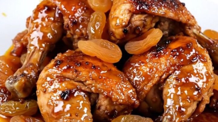 A white round plate featuring tender, slow-cooked chicken thighs glazed with a rich, spiced sauce and golden apricots.