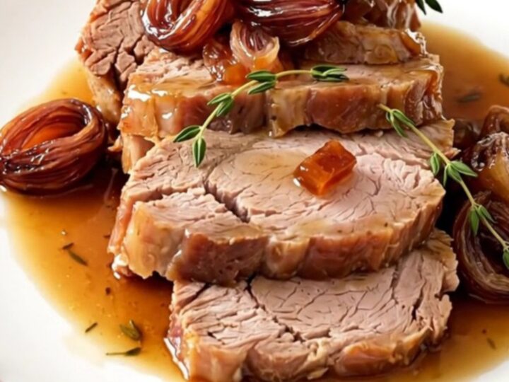 A beautifully plated slice of tender pork roast topped with glossy, caramelized shallots on a white plate.