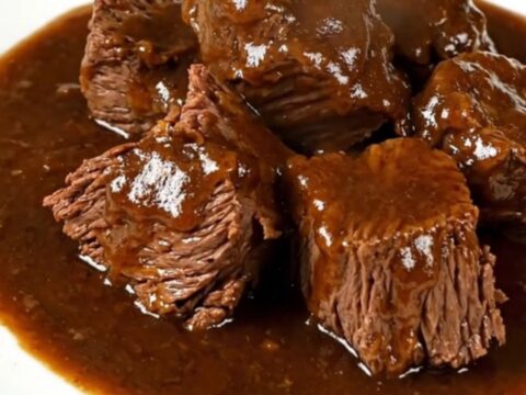 A close-up of a rich, dark beef carbonade stew served in a white bowl, showing tender beef chunks in a glossy gravy.