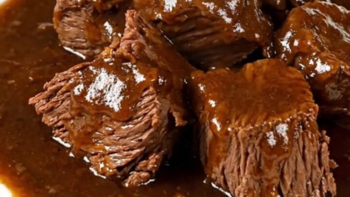 A close-up of a rich, dark beef carbonade stew served in a white bowl, showing tender beef chunks in a glossy gravy.