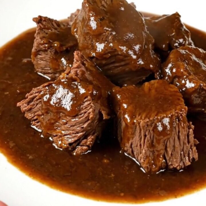A close-up of a rich, dark beef carbonade stew served in a white bowl, showing tender beef chunks in a glossy gravy.