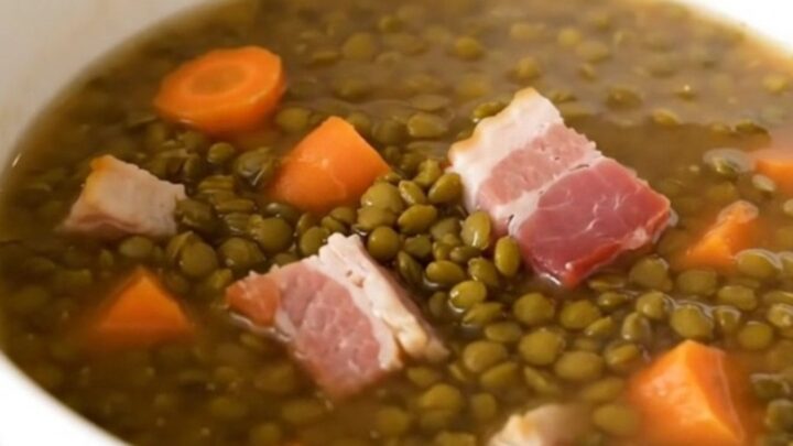 A rustic bowl of lentil and bacon soup served in a white ceramic bowl.