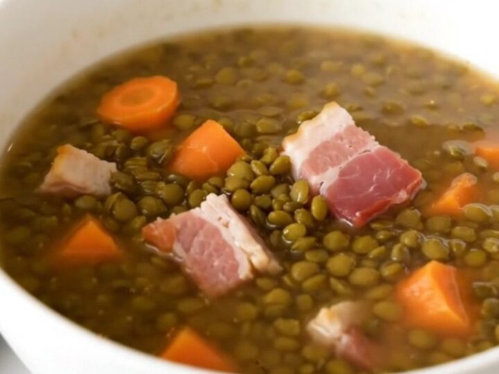 A rustic bowl of lentil and bacon soup served in a white ceramic bowl.