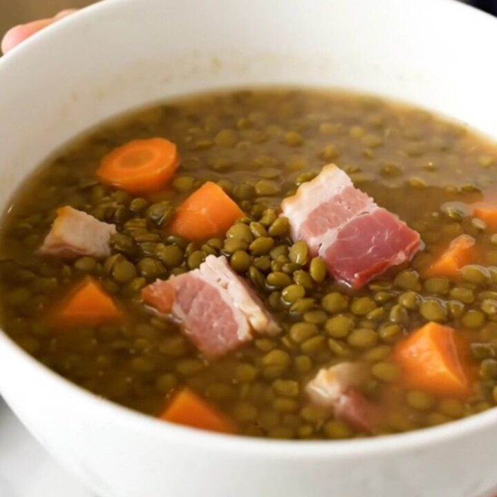 A rustic bowl of lentil and bacon soup served in a white ceramic bowl.
