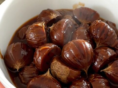 A white bowl filled with glossy, dark red wine stewed chestnuts, carrots, and shallots, steaming slightly.