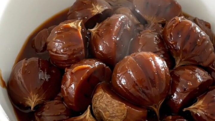 A white bowl filled with glossy, dark red wine stewed chestnuts, carrots, and shallots, steaming slightly.