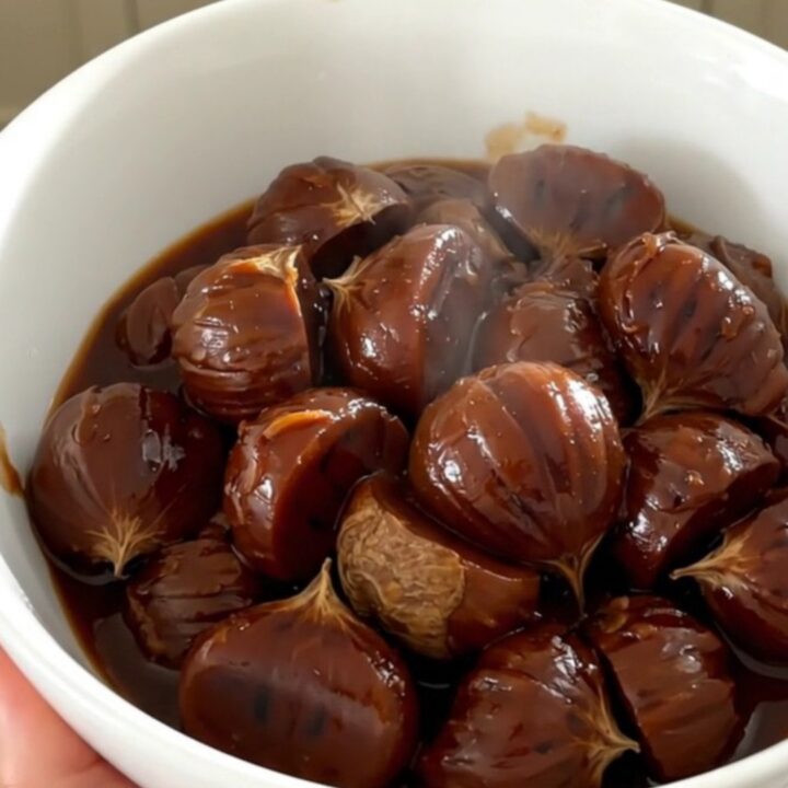 A white bowl filled with glossy, dark red wine stewed chestnuts, carrots, and shallots, steaming slightly.
