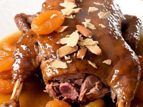 Finished slow-cooked duck legs with apricots and almonds on a white plate.