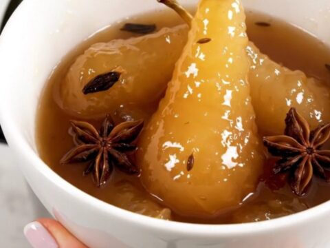 A white bowl filled with glossy, warm pear compote featuring star anise and vanilla bean seeds.