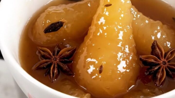 A white bowl filled with glossy, warm pear compote featuring star anise and vanilla bean seeds.