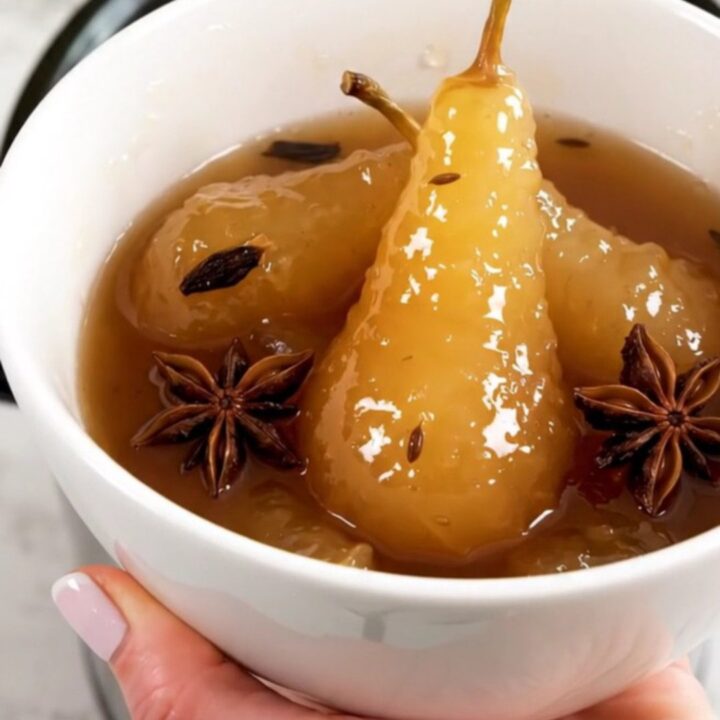 A white bowl filled with glossy, warm pear compote featuring star anise and vanilla bean seeds.