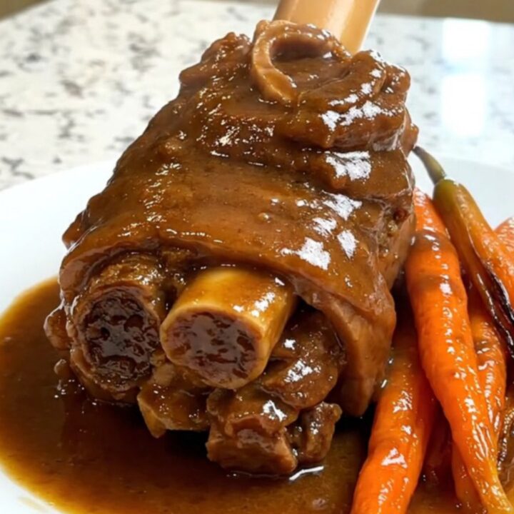 A close-up of tender, glossy lamb neck slices with cooked carrots and rich gravy on a white plate.