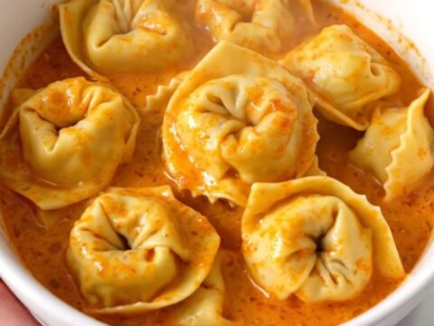 A bowl of creamy tomato tortellini with mascarpone, garnished with herbs in a slow cooker.
