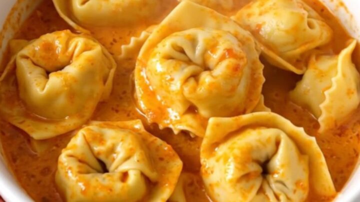 A bowl of creamy tomato tortellini with mascarpone, garnished with herbs in a slow cooker.